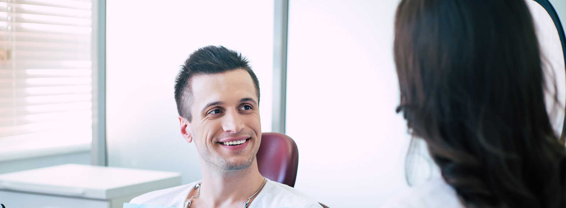 The image shows a man sitting in an office chair with his head turned towards another person who appears to be out of frame, smiling at them.