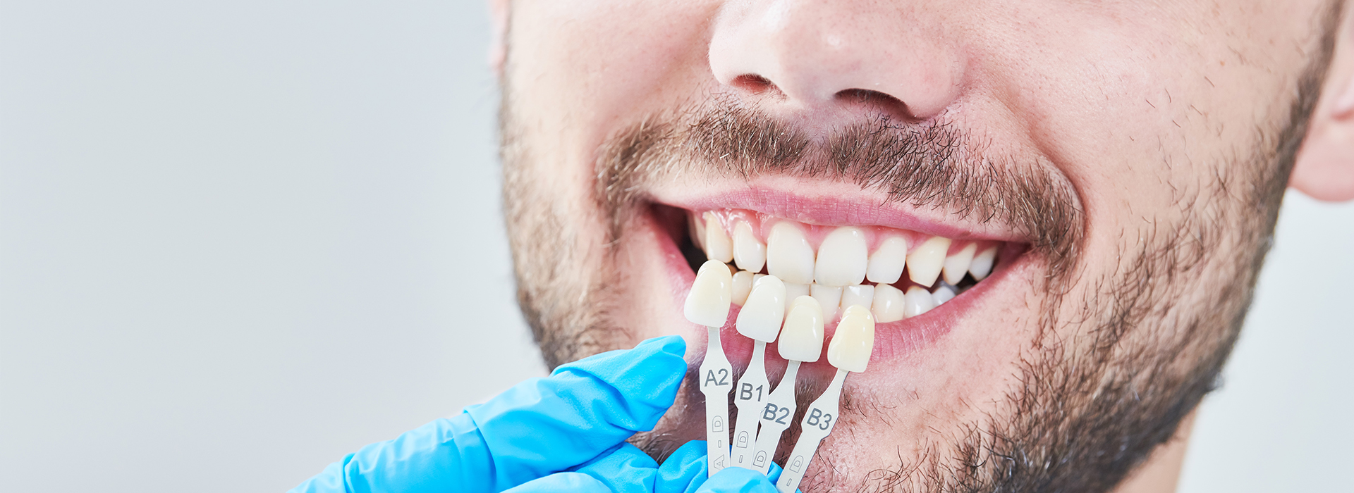 This is a close-up photo of a smiling person with an open mouth, possibly during a dental examination, with a focus on their teeth, showing a toothbrush and dental floss being used by a hand wearing blue gloves.