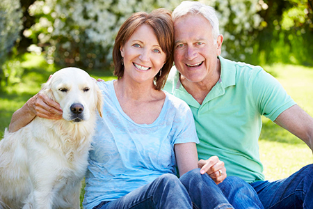 Man and woman sitting outdoors with a yellow labrador retriever between them.