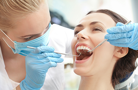 In the image, a dental hygienist is performing a teeth cleaning procedure on a patient at a dental clinic, with both individuals wearing protective gloves and masks.